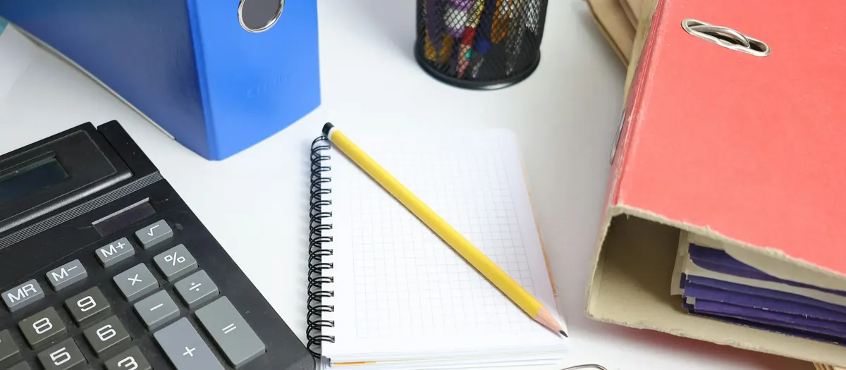 A desk with a calculator, folders and a notebook